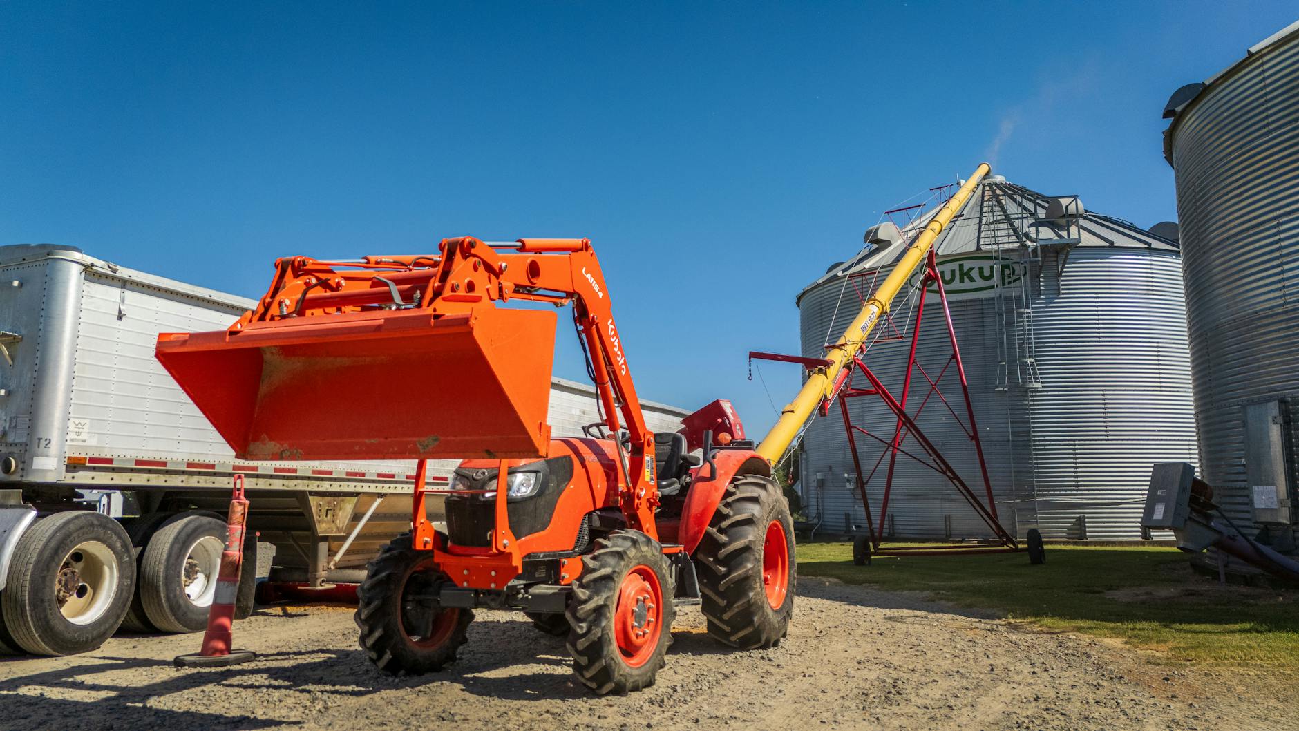Pomarańczowy traktor ze świdrem ślimakowym stoi obok silosów