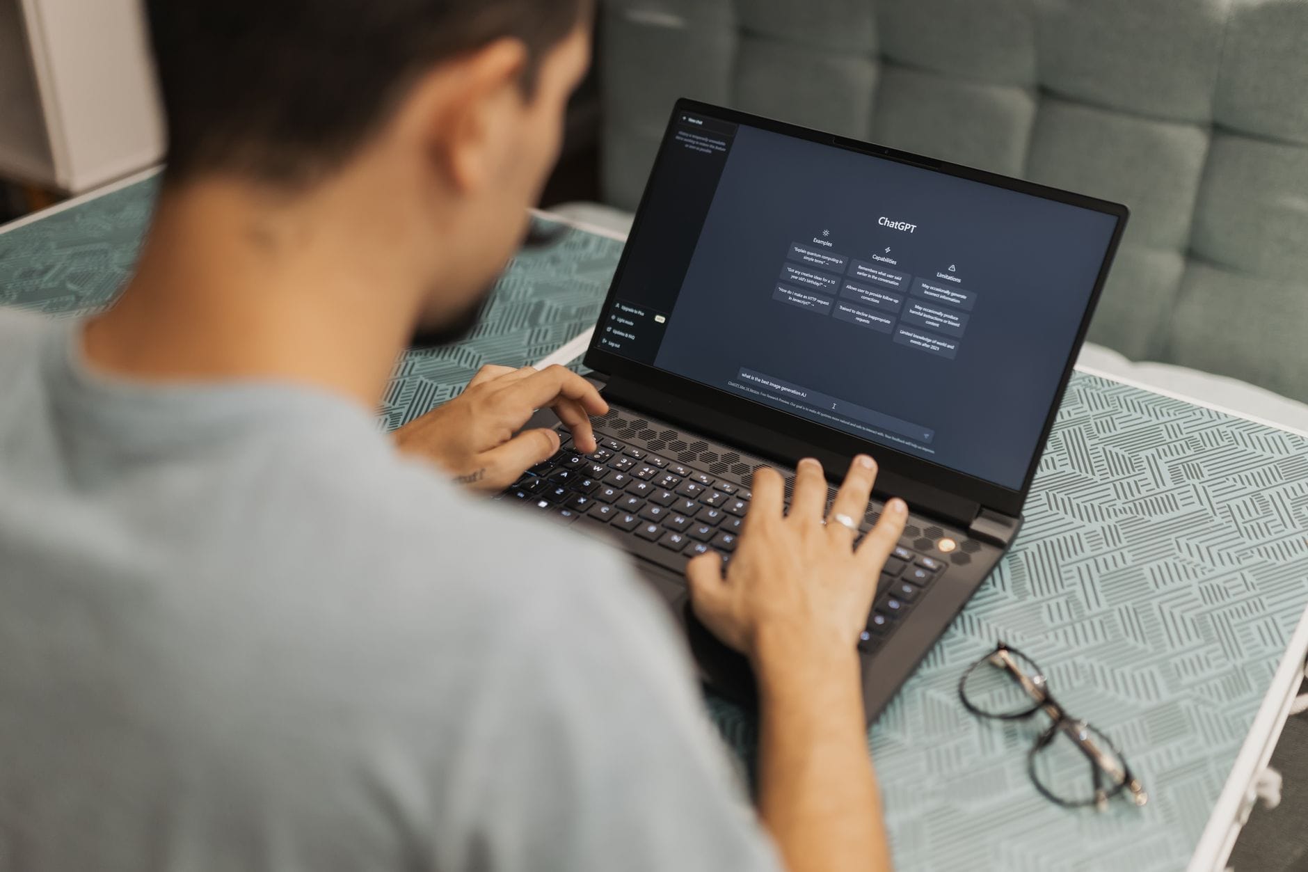 Mężczyzna pracuje przy laptopie z interfejsem AI, okulary leżą obok